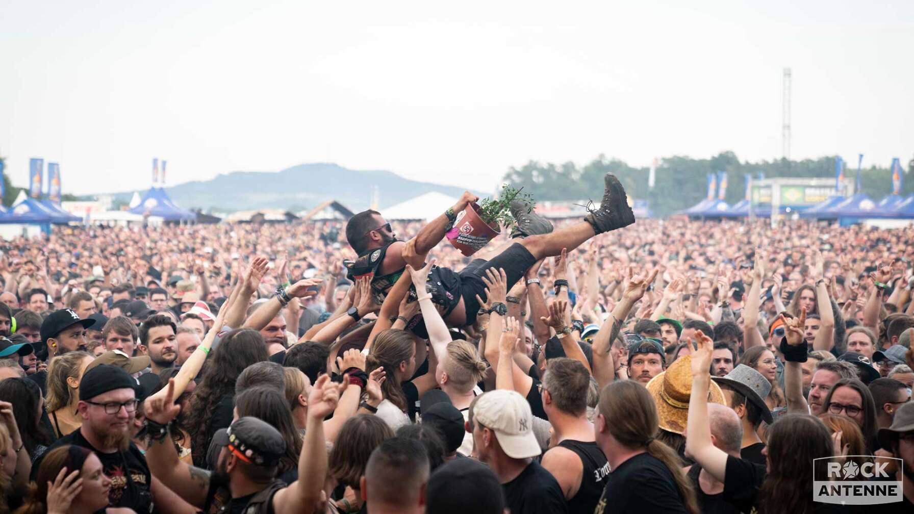 Das Publikum vor der Bühne des Summer Breeze Open Airs. Ein Fan lässt sich von der Menge tragen und hält dabei einen Blumenkübel in der rechten Hand.